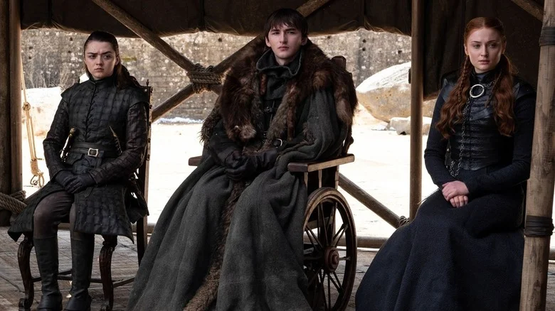 Arya Stark (Maisie Williams), Bran Stark (Isaac Hempstead Wright), and Sansa Stark (Sophie Turner) sit expectantly in Game of Thrones
